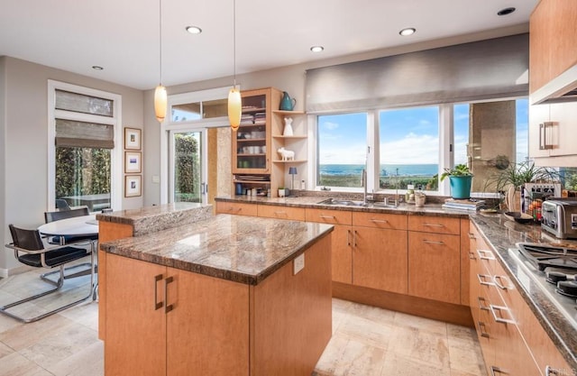 kitchen featuring pendant lighting, stainless steel gas stovetop, sink, dark stone countertops, and a kitchen island