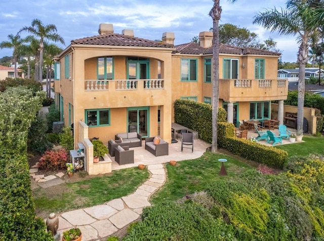 rear view of property featuring a lawn, outdoor lounge area, a balcony, and a patio