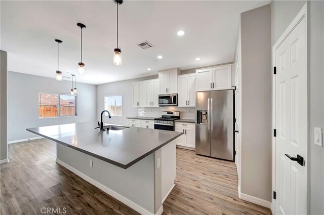 kitchen featuring white cabinets, sink, a center island with sink, decorative light fixtures, and stainless steel appliances