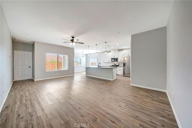 unfurnished living room with ceiling fan, light wood-type flooring, and sink