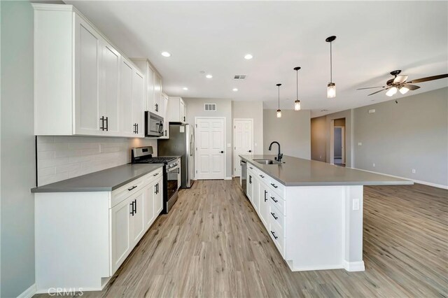 kitchen with pendant lighting, sink, white cabinetry, stainless steel appliances, and a center island with sink