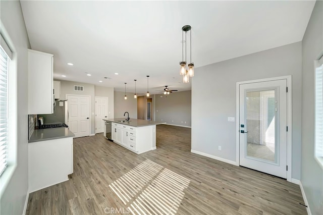 kitchen featuring white cabinets, pendant lighting, light wood-type flooring, a center island with sink, and sink