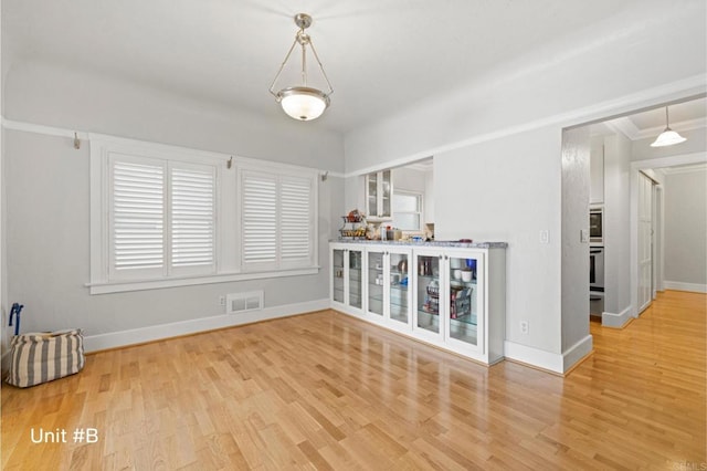 unfurnished room with ornamental molding, light wood-style flooring, visible vents, and baseboards