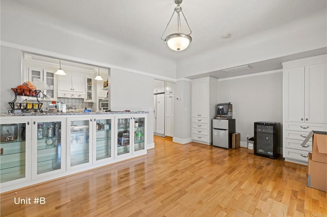 interior space featuring beverage cooler, white refrigerator with ice dispenser, white cabinets, light wood-style flooring, and hanging light fixtures