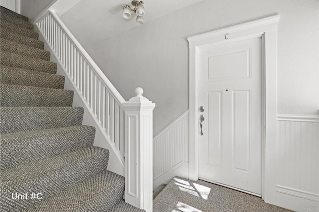 carpeted foyer with wainscoting and stairs