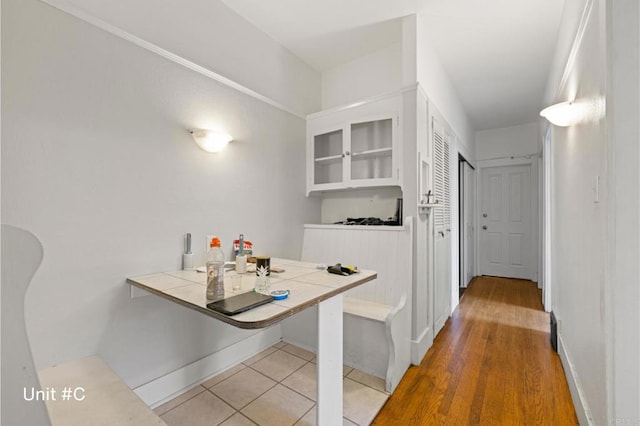 kitchen featuring light tile patterned floors, tile counters, glass insert cabinets, white cabinets, and baseboards