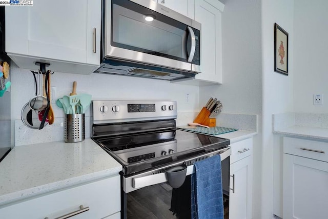 kitchen featuring stainless steel appliances, white cabinets, and light stone counters