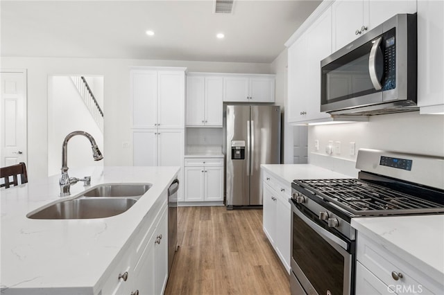 kitchen with appliances with stainless steel finishes, white cabinetry, light stone counters, light hardwood / wood-style flooring, and sink