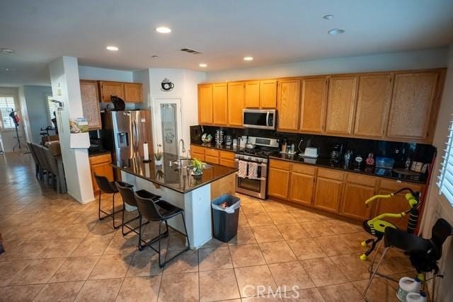 kitchen with sink, stainless steel appliances, tasteful backsplash, a kitchen breakfast bar, and a kitchen island with sink