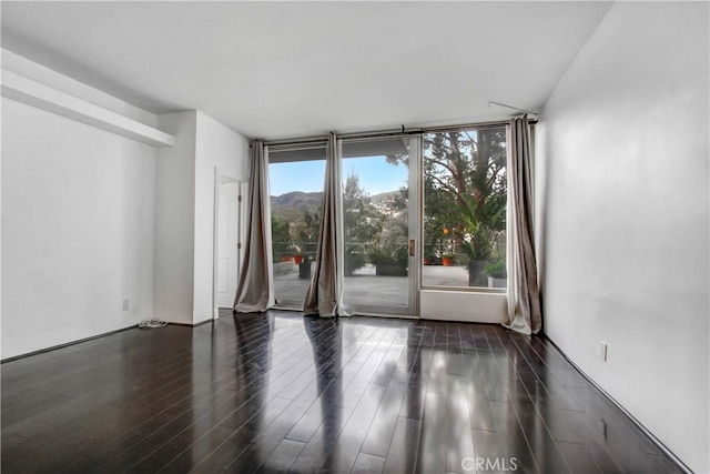 spare room featuring a mountain view, a wall of windows, and dark wood-type flooring