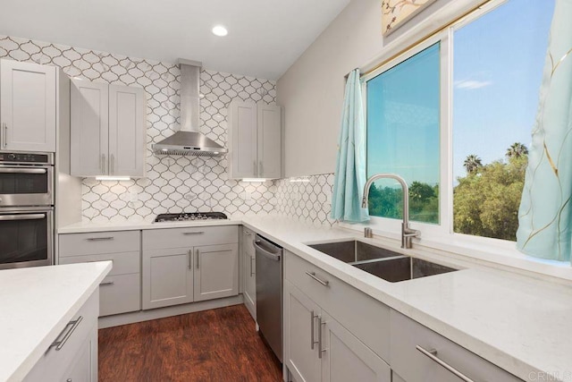 kitchen with wall chimney range hood, stainless steel appliances, decorative backsplash, sink, and dark hardwood / wood-style floors