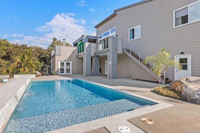 rear view of property with pool water feature, french doors, a patio area, and a balcony