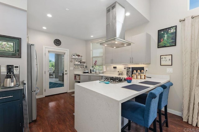 kitchen with kitchen peninsula, island exhaust hood, appliances with stainless steel finishes, a breakfast bar area, and white cabinets