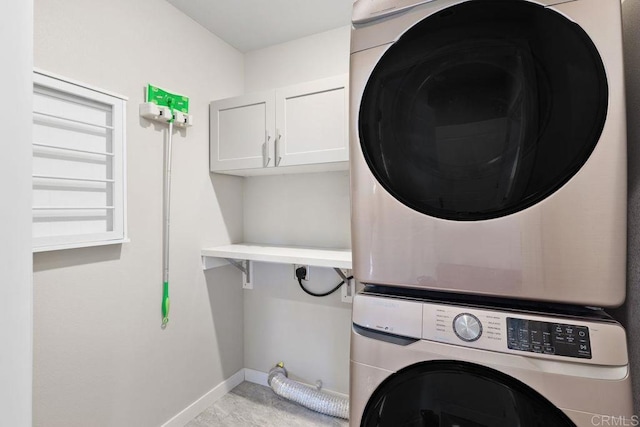 clothes washing area featuring cabinets and stacked washer and clothes dryer