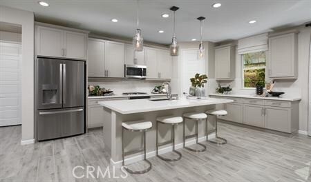 kitchen featuring hanging light fixtures, a kitchen island with sink, stainless steel appliances, light wood-type flooring, and a kitchen bar