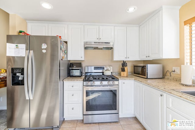 kitchen featuring light stone countertops, stainless steel appliances, white cabinets, and light tile patterned flooring