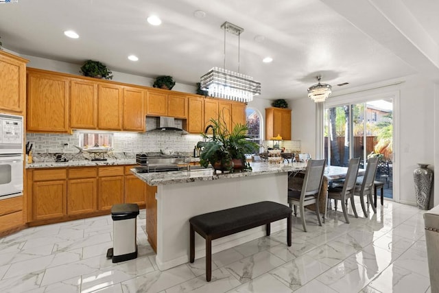 kitchen with light stone counters, ventilation hood, a kitchen island, white appliances, and backsplash