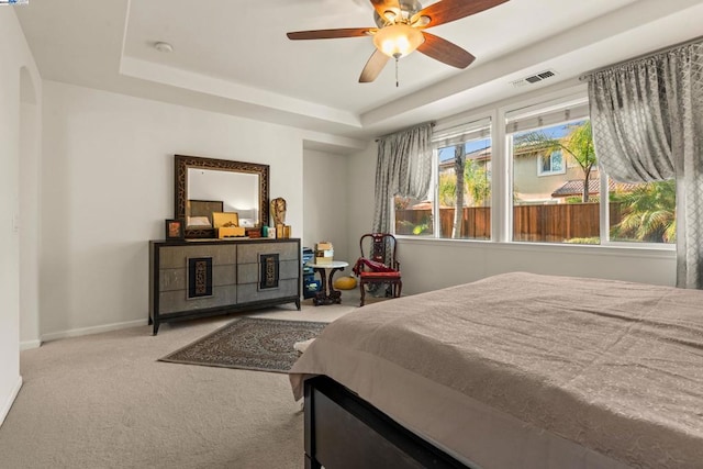 bedroom with ceiling fan, light colored carpet, and a raised ceiling