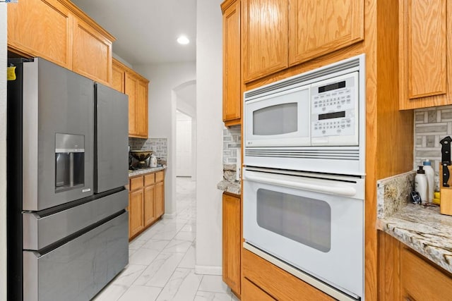 kitchen featuring light stone counters, backsplash, and white appliances