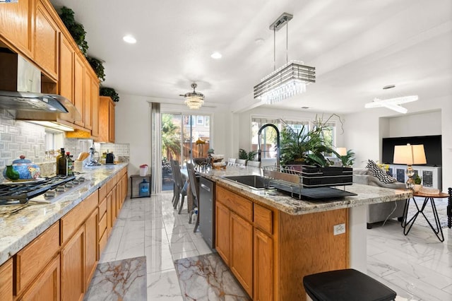 kitchen with appliances with stainless steel finishes, decorative backsplash, light stone counters, a center island with sink, and sink