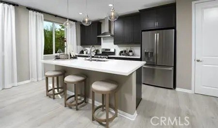 kitchen featuring a kitchen bar, hanging light fixtures, wall chimney range hood, a center island with sink, and stainless steel fridge