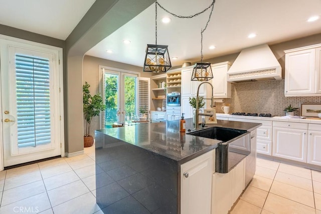 kitchen with white cabinetry, a kitchen island with sink, pendant lighting, and custom range hood