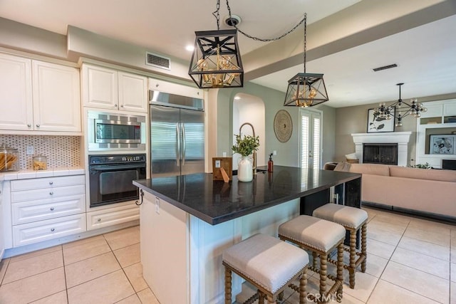 kitchen featuring tasteful backsplash, light tile patterned floors, built in appliances, decorative light fixtures, and a center island