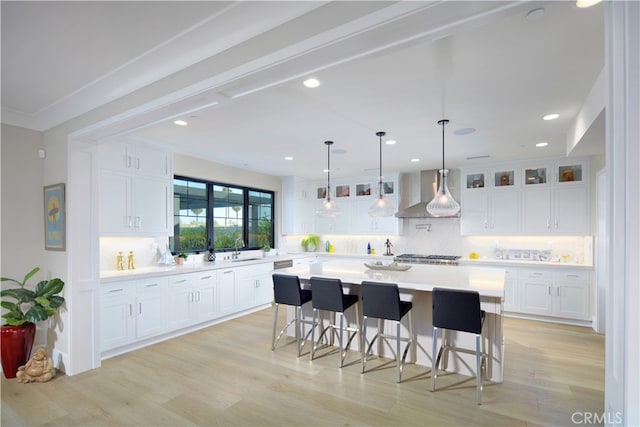 kitchen featuring light wood-type flooring, white cabinetry, and wall chimney range hood