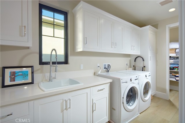 clothes washing area featuring separate washer and dryer, cabinets, light hardwood / wood-style floors, and sink