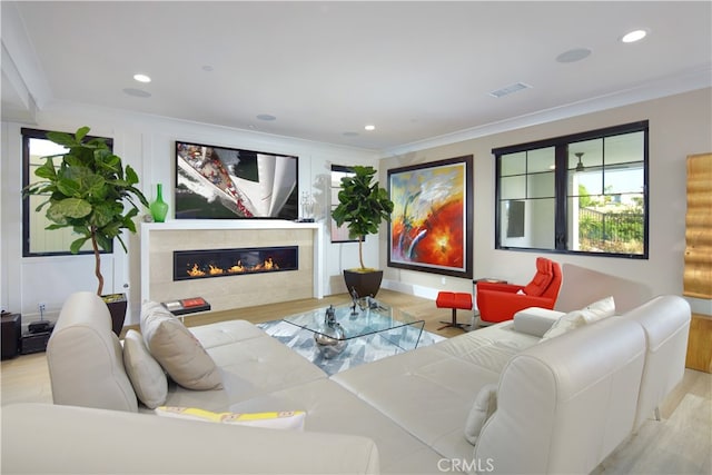 living room featuring light hardwood / wood-style floors, ornamental molding, and a tiled fireplace