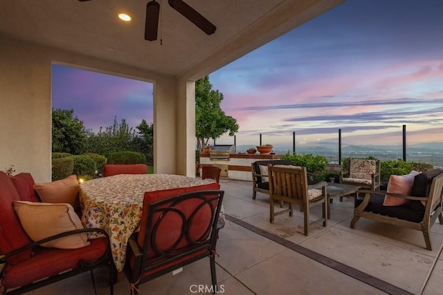 patio terrace at dusk with ceiling fan, grilling area, exterior kitchen, and an outdoor living space