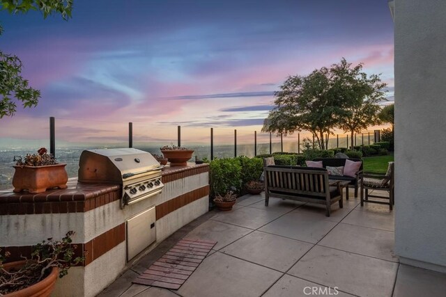 patio terrace at dusk with an outdoor kitchen, grilling area, outdoor lounge area, and a water view