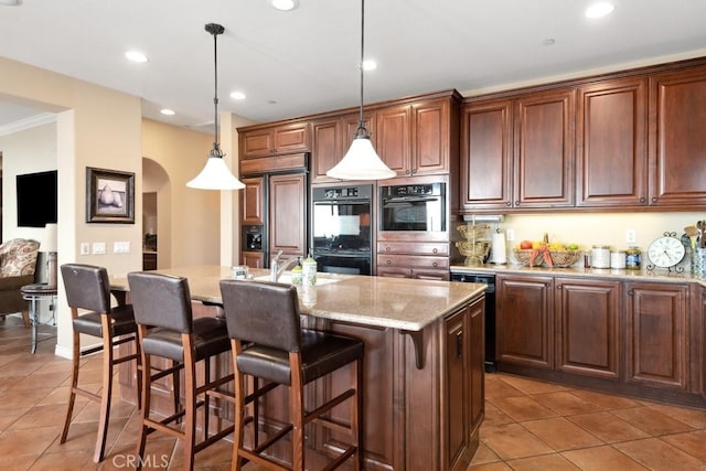 kitchen with paneled built in refrigerator, tile patterned flooring, a center island with sink, hanging light fixtures, and black double oven