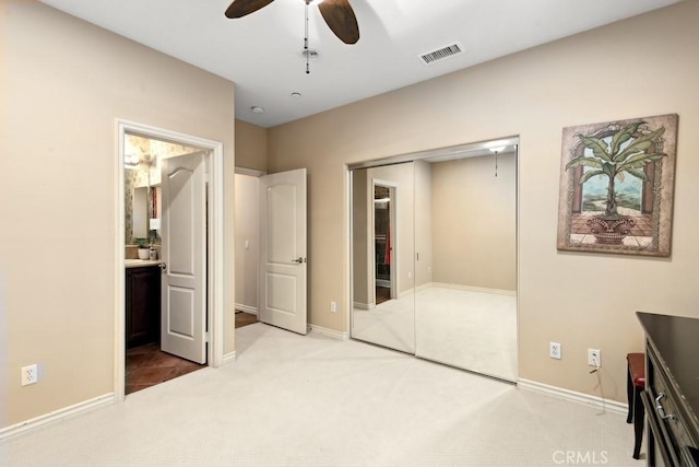 unfurnished bedroom featuring ensuite bathroom, light colored carpet, ceiling fan, and a closet