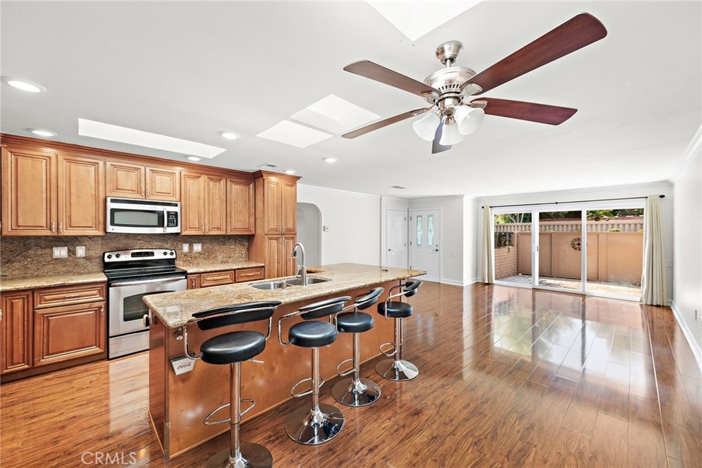 kitchen featuring a skylight, stainless steel appliances, sink, a center island with sink, and a breakfast bar area