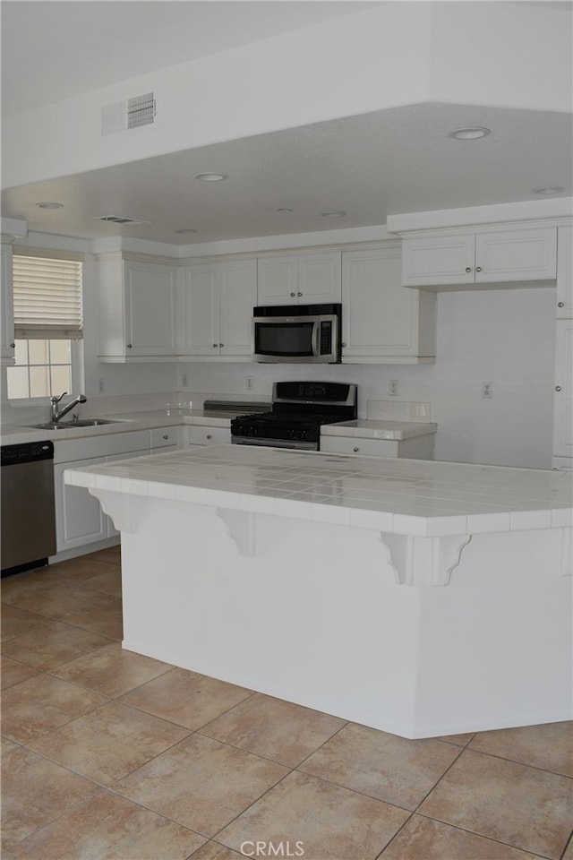 kitchen with white cabinets, light tile patterned floors, sink, appliances with stainless steel finishes, and a breakfast bar area