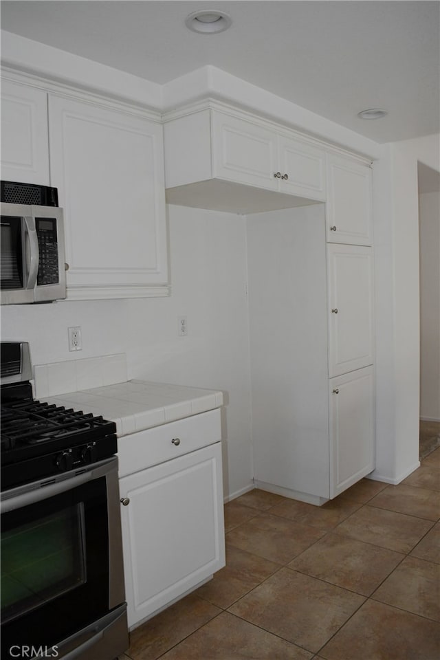 kitchen featuring stainless steel appliances, white cabinets, tile countertops, and light tile patterned flooring