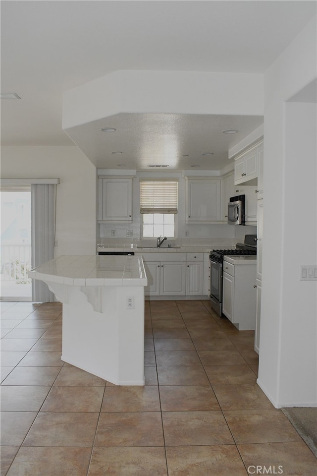 kitchen featuring sink, white cabinetry, a kitchen bar, tile countertops, and gas range