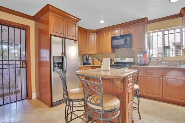 kitchen featuring a breakfast bar, stainless steel fridge, light stone countertops, range with gas stovetop, and a kitchen island