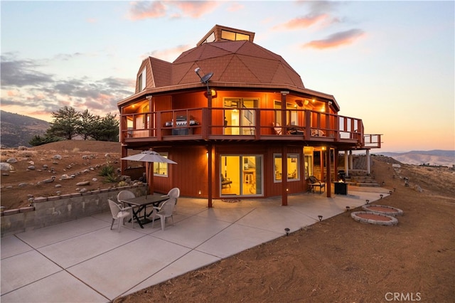 back house at dusk featuring a patio, a balcony, and a mountain view