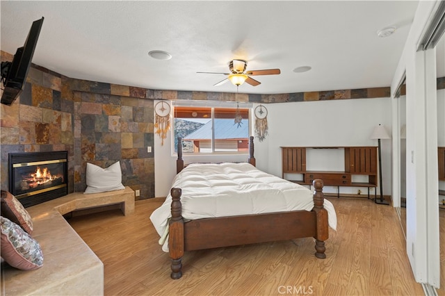 bedroom featuring light hardwood / wood-style floors, a tile fireplace, and ceiling fan