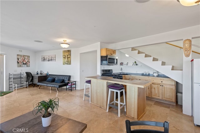 kitchen with gas stove, white refrigerator, light brown cabinets, and a kitchen breakfast bar