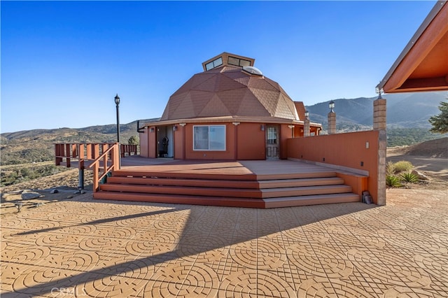 rear view of property with a deck with mountain view and a patio