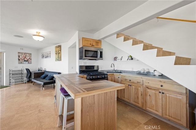 kitchen with beamed ceiling, light brown cabinetry, black range with gas cooktop, a kitchen bar, and a center island