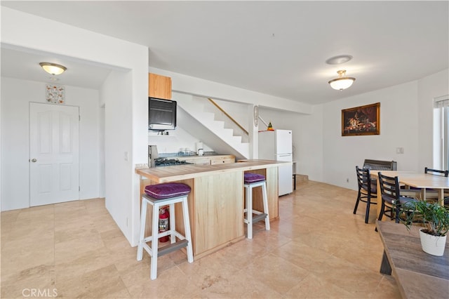 kitchen with wooden counters, stainless steel range oven, kitchen peninsula, white refrigerator, and a kitchen breakfast bar