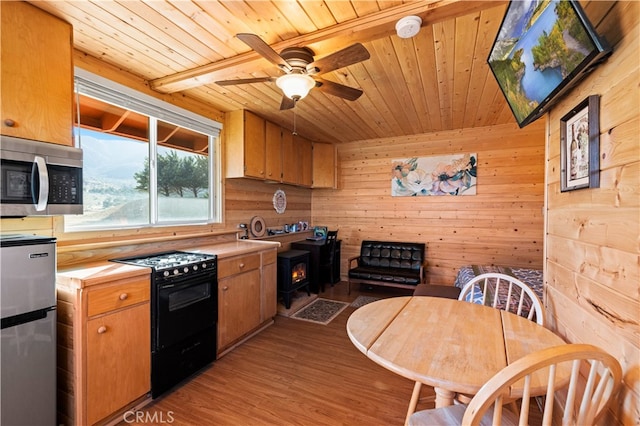 kitchen with wood walls, light wood-type flooring, ceiling fan, wood ceiling, and appliances with stainless steel finishes