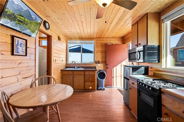 kitchen with sink, black gas range, wood-type flooring, wooden walls, and wooden ceiling