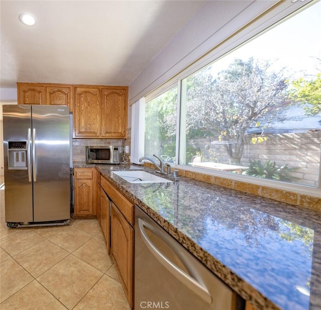 kitchen with appliances with stainless steel finishes, sink, dark stone counters, and light tile patterned floors