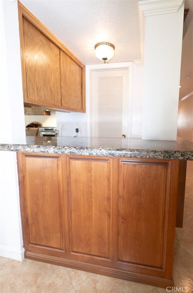 kitchen with stone countertops, light tile patterned floors, and kitchen peninsula