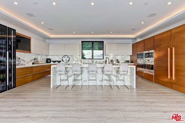 kitchen featuring decorative backsplash, a large island with sink, white cabinetry, and a breakfast bar